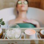 Self-Love Bisa Membuat Kulit Lebih Sehat? Cek Faktanya! Woman relaxing in a bathtub with a candle and plants, enjoying a serene spa experience.